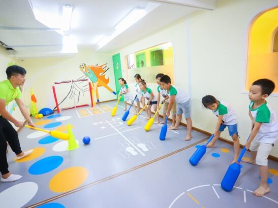 Bambini in età prescolare giocano con mazze e palline colorate in un'aula decorata con colori vivaci.