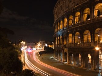 Vista notturna del Colosseo a Roma con scie luminose prodotte dalle auto sulla strada sottostante.